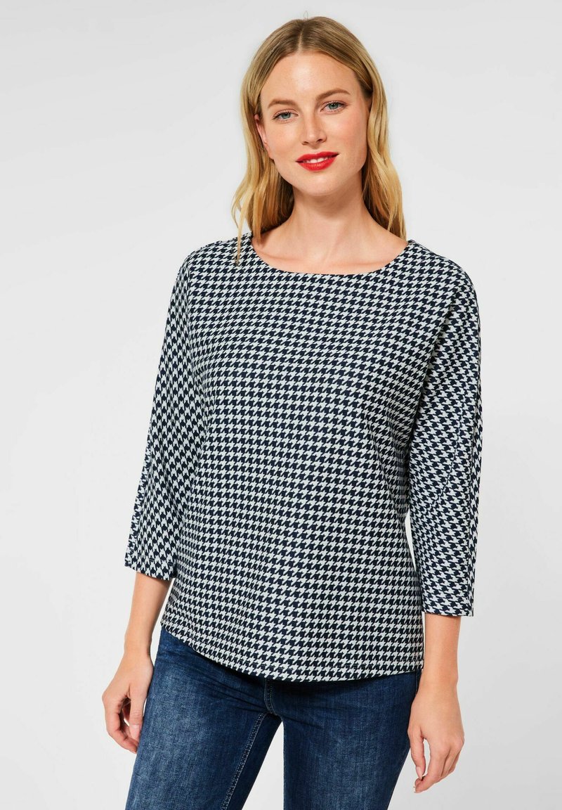 Top con motivo a quadri houndstooth navy e bianco, con maniche a tre quarti, scollo rotondo e vestibilità comoda, abbinato a jeans blu scuro.