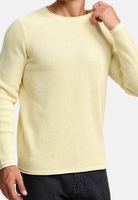 Pull long à manches longues tricoté jaune, texturé, avec un col rond et des poignets côtelés, associé à un jean noir.
