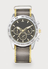 Chronografur med sort urskive, sølv bezel, gule detaljer og et struktureret gråt stofarmbånd. Har tachymeter og flere subskiver.