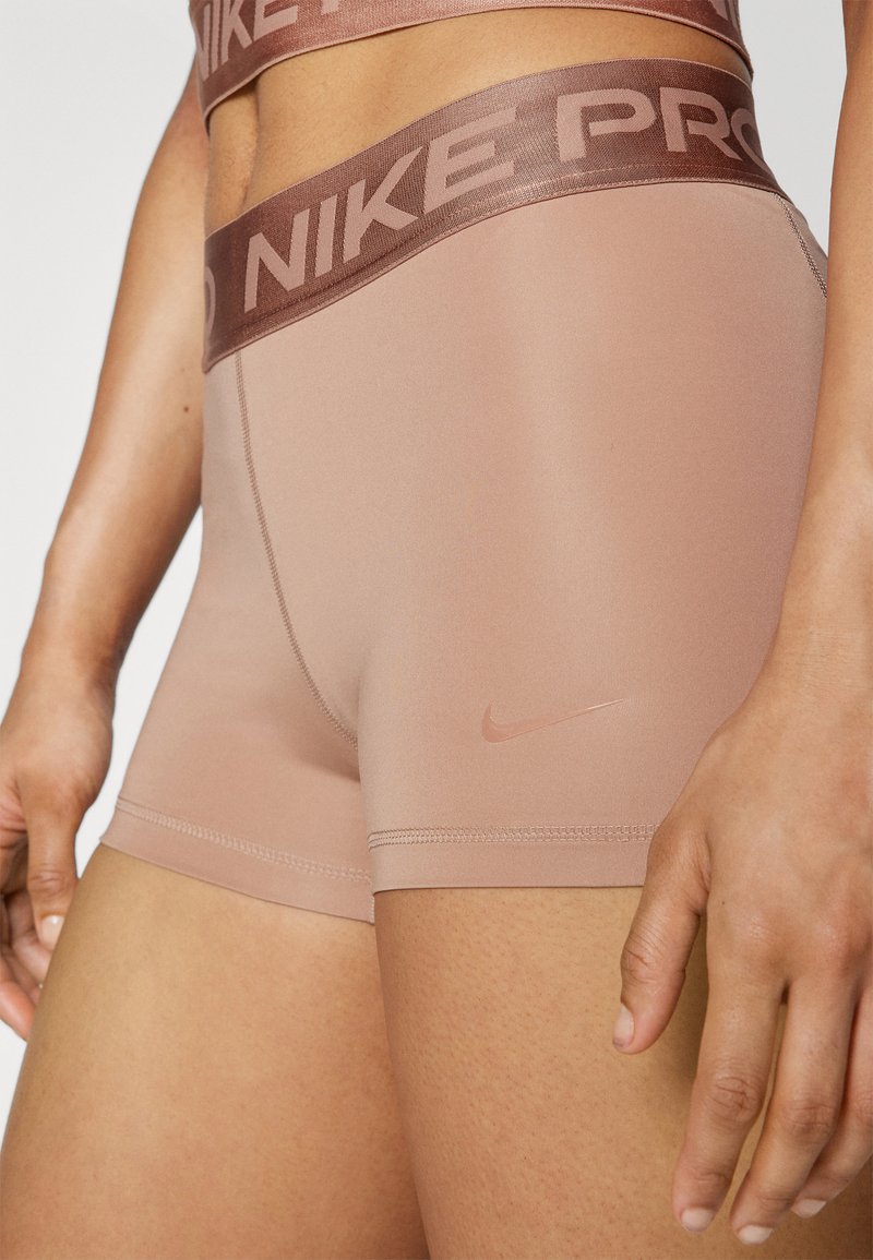 Shorts Nike Pro color beige chiaro con un ampio elastico marrone con il marchio. Presentano una texture liscia e un piccolo logo sul lato inferiore.