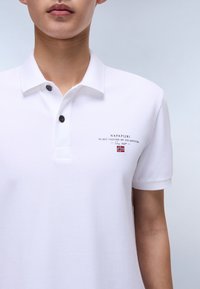 Hvid polo t-shirt lavet af tekstureret stof, med en to-knaps knaplukning, korte ærmer og mærkning med broderede detaljer på brystet.