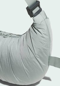 Borsa a tracolla imbottita verde chiaro con tessuto strutturato, forma curva, tracolla regolabile e fibbia in plastica. Dettagli di cuciture evidenti.