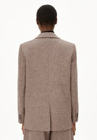 Bruine gestructureerde blazer met een op maat gemaakte pasvorm, notch-lapel en twee-knopen sluiting. Kenmerken zijn subtiele patronen en knoopmanchetten.