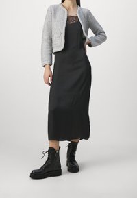 Veste cropped en tweed gris sur une robe midi en satin noir, associée à des bottines noires en cuir à lacets avec des semelles texturées.