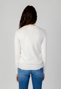 Maglione bianco a maniche lunghe realizzato in un tessuto leggero e morbido, con un design aderente e orlo a coste, abbinato a jeans in denim blu.