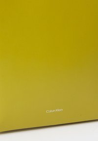 Prodotto Calvin Klein in un vivace verde oliva, texture liscia, design minimalista, con il nome del marchio visibile in testo bianco.