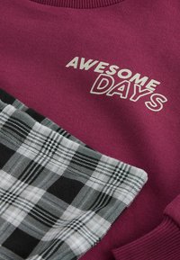Bordowy sweatshirt z napisem "WSPANIAŁE DNI" w kolorze białym. Posiada czarno-białą nakładkę w kratkę na dolnej części. Miękka tekstura.