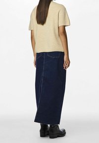 Beżowa, prążkowana dzianinowa bluzka z krótkim rękawem w zestawieniu z granatową, długą spódnicą dżinsową z dwoma tylnymi kieszeniami i bocznym rozcięciem, noszona z czarnymi botkami za kostkę.