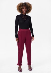 Haut noir à manches longues avec empiècement en dentelle à pois transparents, associé à un pantalon bordeaux taille haute. Talons hauts bordeaux brillants, jambes de pantalon à revers.