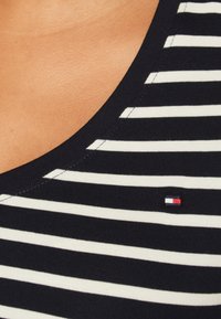 Top a canotta a righe blu navy e bianche con scollo arrotondato. Presenta un piccolo logo colorato sul petto e una texture a coste.