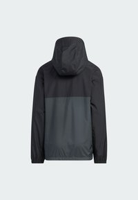 Chaqueta con capucha resistente al agua que presenta una sección superior negra, una sección inferior gris y puños elásticos, con una textura suave y un diseño minimalista.