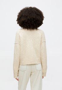 Beige zkrácený svetr s měkkou texturou, raglánovými rukávy a žebrovaným pasem, nošený přes světlé kalhoty.