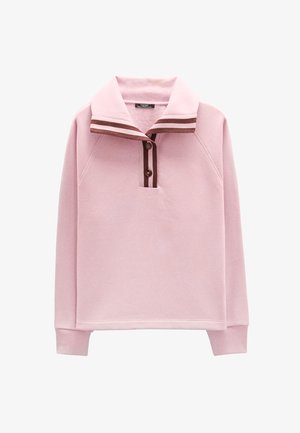 Jasnoróżowy sweter z założonym kołnierzem zdobionym brązowymi paskami, trzema guzikami oraz rękawami raglanowymi. Miękka tekstura.