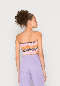 Top cropped sem alças com padrão zigzag multicolorido em laranja, rosa e preto; combinado com calças largas em lavanda clara.