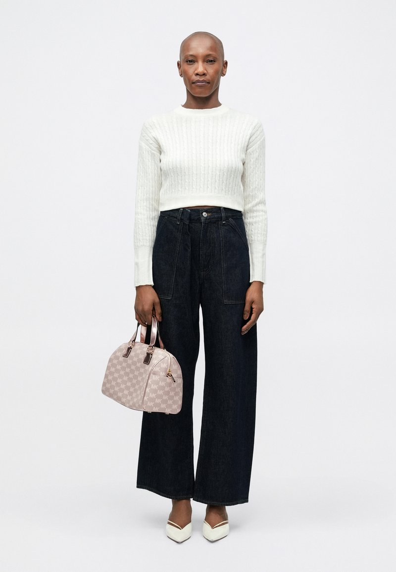 Pull court côtelé blanc, jean large foncé, sac à main à motifs rose clair avec matériel doré, et escarpins blancs à bout pointu.