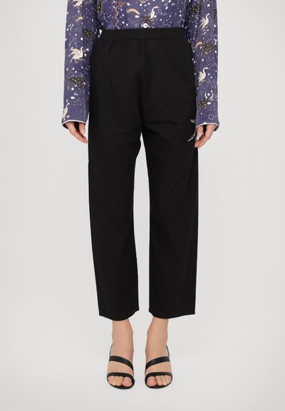 Pantalones negros de talle alto y pernera cónica con cinturilla elástica. Combinados con una camisa de manga larga de rayas azul marino y sandalias negras con tiras.