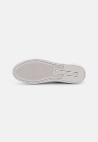 Suola di sneaker bianca, in gomma liscia con un motivo di presa testurizzato, marchio in rilievo e bordi arrotondati. Design pulito e minimalista.