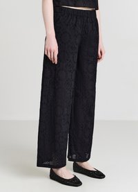 Schwarze, weit geschnittene Hose mit filigraner Blumenstickerei und kleinen Ausschnitten. Weicher Stoff mit elastischem Bund für Komfort.