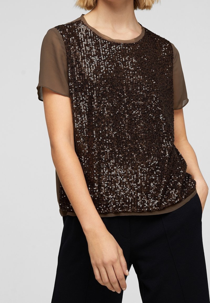 Top marrone con paillettes, maniche corte e trasparenti; scollatura rotonda; e vestibilità ampia. Le paillettes creano un effetto texture e luccicante.