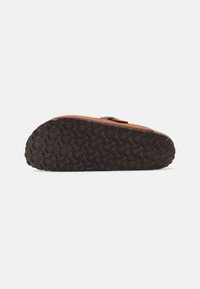 Sándala de cuero marrón con suela de goma negra que presenta un patrón de banda de rodadura ondulado y una correa ajustable en la parte superior.