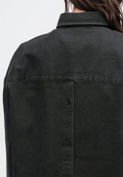 Ciemna koszula dżinsowa z ostrym kołnierzem, z zapięciem na guziki z tyłu i miękkim, teksturowanym wykończeniem.