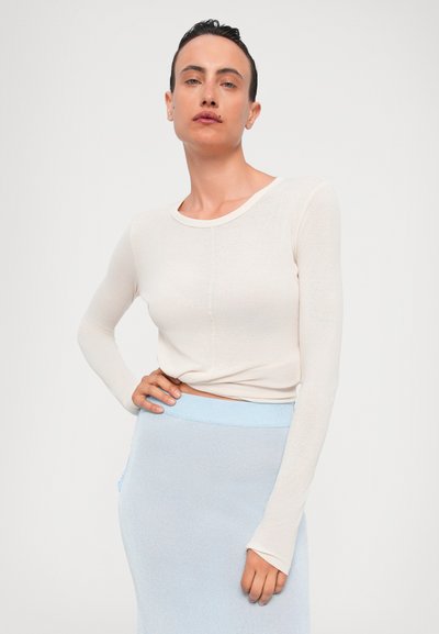 Top creme de manga longa, ajustado, feito de tecido leve, com um decote redondo e detalhes sutis nas costuras. Combina com uma saia de malha azul clara.