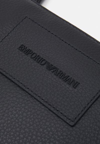 Černá kožená taška s texturovaným povrchem, embosovaným logem "Emporio Armani" a obd�élníkovou nálepkou.