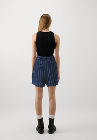 Czarna bezrękawnikowa bluzka w połączeniu z niebieskimi szortami w prążki. Szorty mają tylne kieszenie i wysoką talię. Czarne botki za kostkę i białe skarpetki.