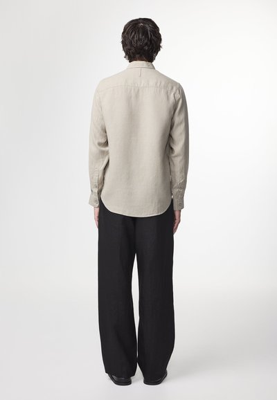 Beige linen shirt with long sleeves and a rounded hem, paired with wide black trousers. Features button cuffs and a stitched collar.