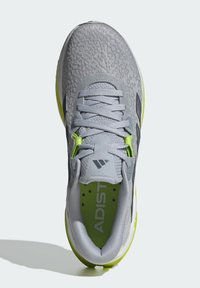 Zapato deportivo gris con parte superior texturizada, acentos verdes y suela acolchada. Cuenta con un cierre de cordones y una puntera reforzada.