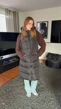 Ilgas juodas pūkinis paltas su aukštu apykakliu, turintis užtrauktuką priekyje ir horizontalius siūlius. Dėvimas ant rudų ilgų rankovių marškinėlių ir šviesiai mėlynų džinsų.