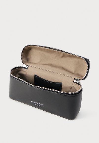 Μαύρη θήκη Emporio Armani με φερμουάρ, ανοιχτή για να εμφανιστεί η μπεζ επένδυση στο εσωτερικό και μια μικρή εσωτερική τσέπη, τοποθετημένη σε ανοιχτό φόντο.