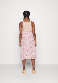 Camisola bege de alças combinada com uma saia midi floral em tons de rosa, branco e amarelo, apresentando um design folgado e uma textura suave.