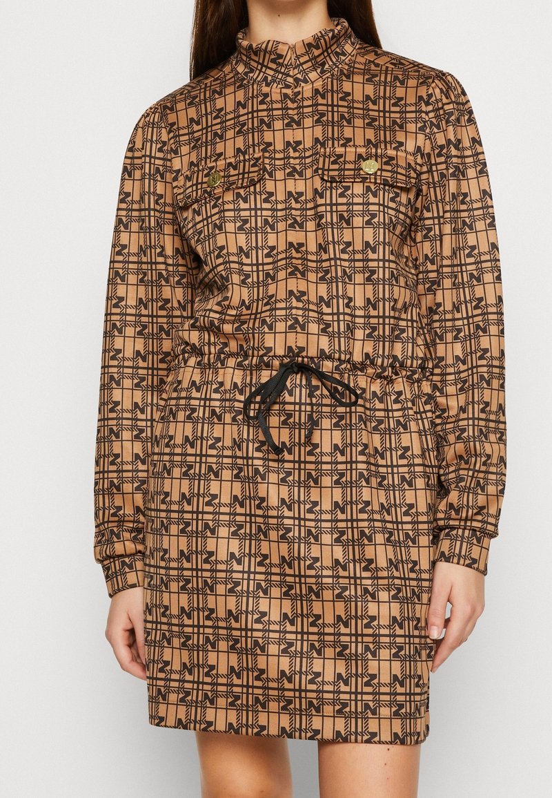Robe à manches longues en tissu marron avec un motif géométrique noir. Elle présente un col montant, une taille élastique et des poches avant avec des boutons dorés.