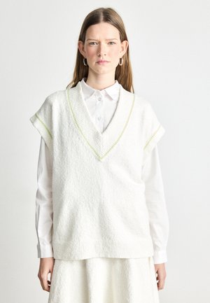 Witte gebreide vest met V-hals, korte mouwen en lichtgroene accenten langs de halslijn, gecombineerd met een wit overhemd met kraag.