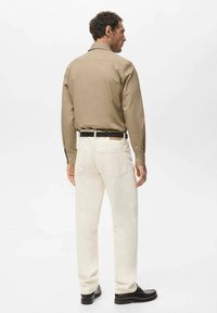 Camisa marrón clara con cuello, combinada con jeans blancos y zapatos negros. La camisa es de manga larga con puños de botón; los jeans tienen bolsillos traseros.