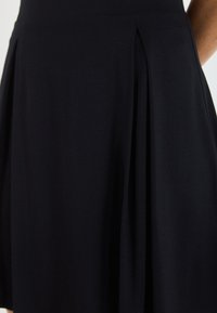 Zwarte gepliseerde rok met een gladde textuur, middellange snit, met scherpe messpleats voor extra beweging en structuur.
