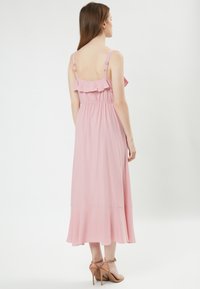 Vestido maxi rosa con un respaldo con volantes, tirantes ajustables, cintura elástica y dobladillo fluido, hecho de una tela ligera.