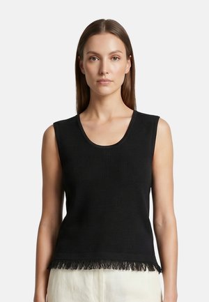 Donna che indossa un top nero senza maniche a coste con scollo rotondo e orlo sfrangiato, abbinato a pantaloni chiari.