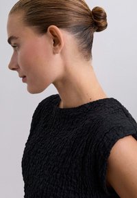 Top nero strutturato con scollo rotondo e maniche corte, caratterizzato da un tessuto arricciato che aggiunge profondità e dimensione.