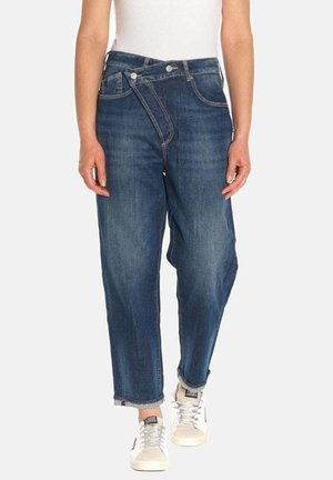 Dunkelblaue Denim-Jeans mit lockerer Passform, die ein einzigartiges schräges Reißverschlussdesign, umgekrempelte Säume und weiße Sneakers kombinieren.