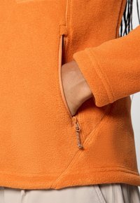 Oranger Fleece-Pullover mit Reißverschlusstasche und strukturiertem Stoff. Das Design umfasst einen hohen Kragen und gerippte Ärmel.