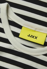 T-shirt à rayures noir et blanc avec un col rond et une étiquette jaune vif portant "JJXX" en texte noir. Matériau en coton texturé.