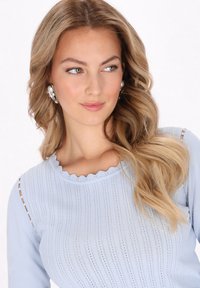 Top a costine blu chiaro con scollatura ondulata, caratterizzato da righe verticali e sottili aperture sulle spalle. Tessuto liscio, design aderente.