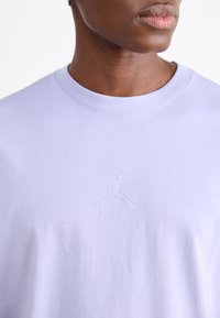 Lyslilla bomulds t-shirt med rund halsudskæring og et præget Jumpman-logo med "AIR" tekst på brystet. Glat overflade.