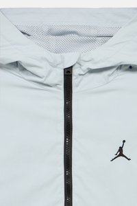 Ανοιχτό γκρι μπουφάν με κουκούλα, μαύρο φερμουάρ μπροστά και μαύρο κεντημένο λογότυπο Jumpman στο αριστερό στήθος.