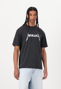 Must t-särk lühikeste varrukatega, must, millel on valge "METALLICA" graafiline logo julge fondiga, ümmargune kaelus ja mugav lõige.