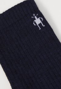 Calcetines de rayas azul marino con una textura suave, que presentan un pequeño logo blanco en el costado, mostrando un diseño de personaje, lo que aumenta el interés visual.