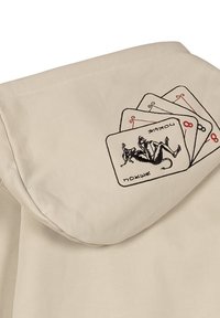 Prenda beige con capucha que presenta un diseño bordado de cartas de juego con un personaje, y acentos en negro y rojo en los bordes de las cartas.