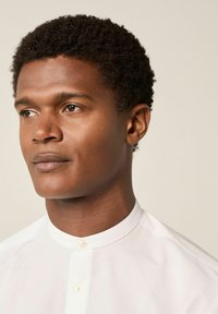 Camisa de cuello blanco con cierre de botón, que presenta una textura suave y un diseño minimalista, llevada por una persona con cabello corto y rizado.
